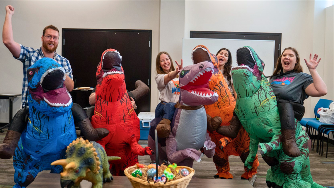This is an image of library staff jumping while wearing dinosaur costumes for Summer Reading 2026
