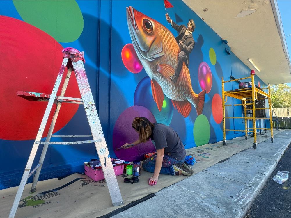 Artist working on an outdoor mural of fish and bubbles.