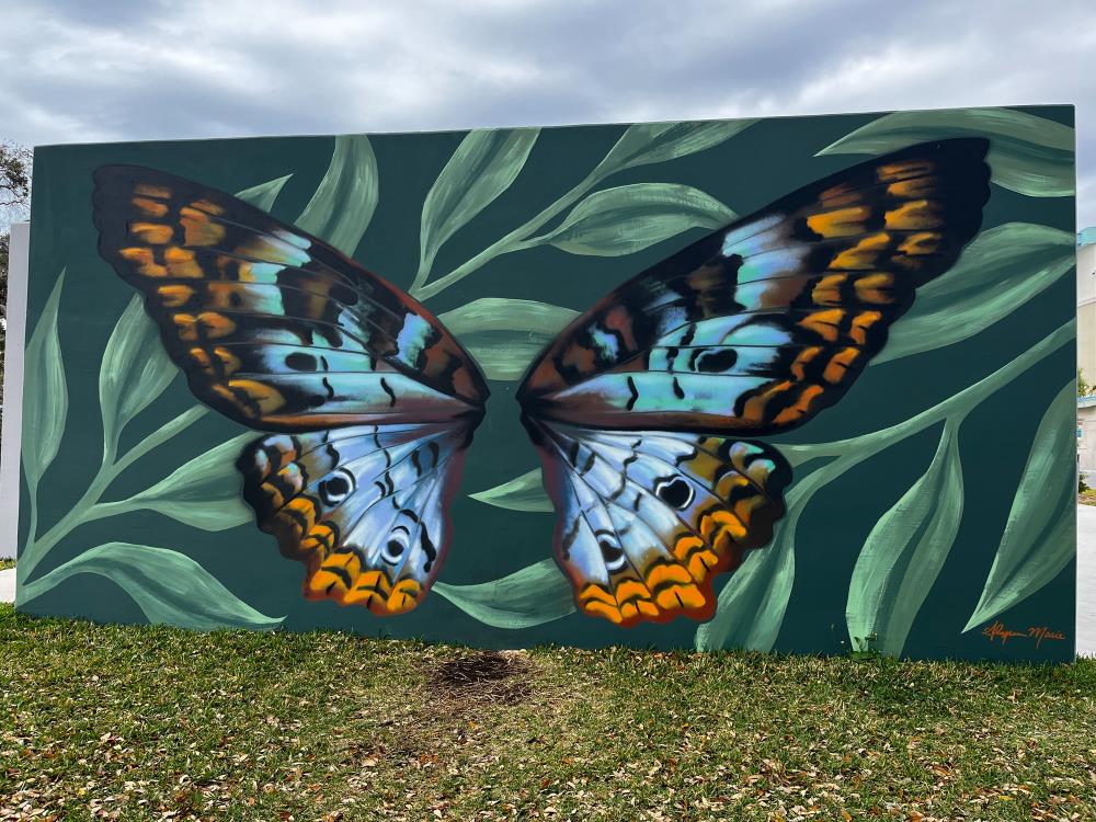 External wall mural of a butterfly on green leaves.