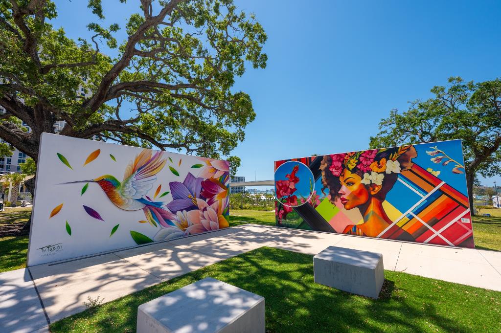 Two outside wall murals in a park, one with humming birds.