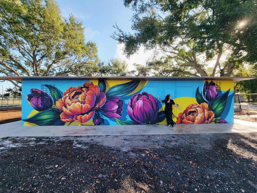 Woman with outstretched arms posing in front of floral mural outdoors.