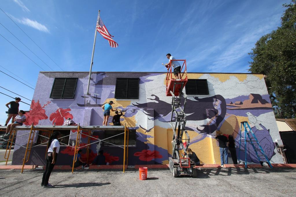 Half a dozen artists painting an outdoor mural.