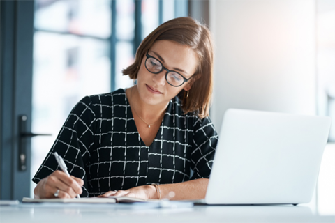 Woman sitting at a desk with a laptop writing.