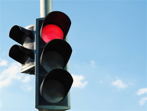 Traffic signal with red light lit and blue sky behind.