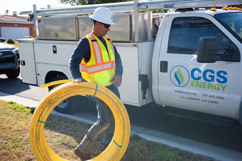Man in hard hat and high visibility vest with a roll of yellow cable.