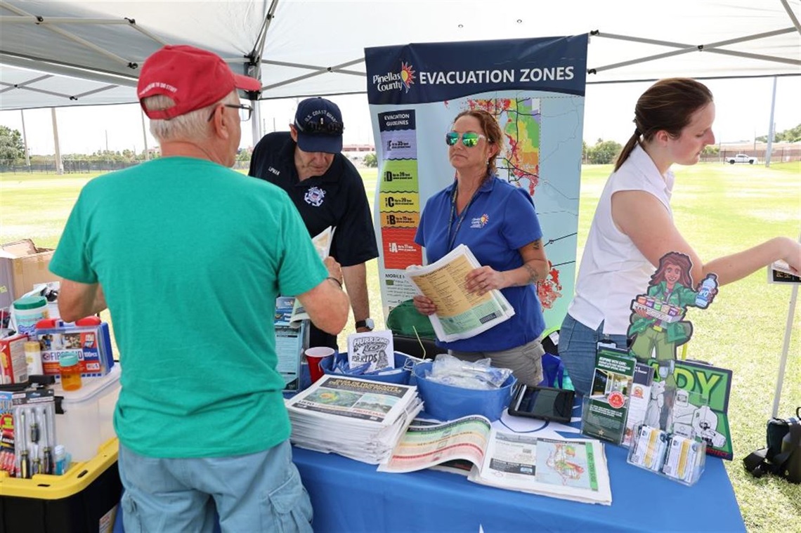 People under a tent with hurricane preparedness information on a table.