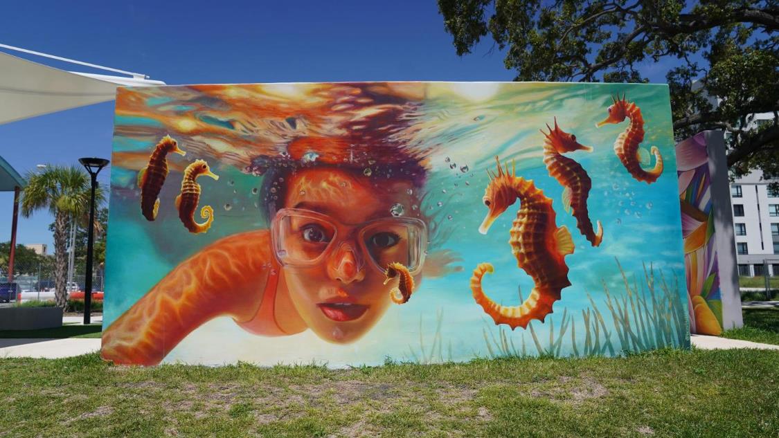 Outdoor wall mural of a girl swimming underwater with seahorses.