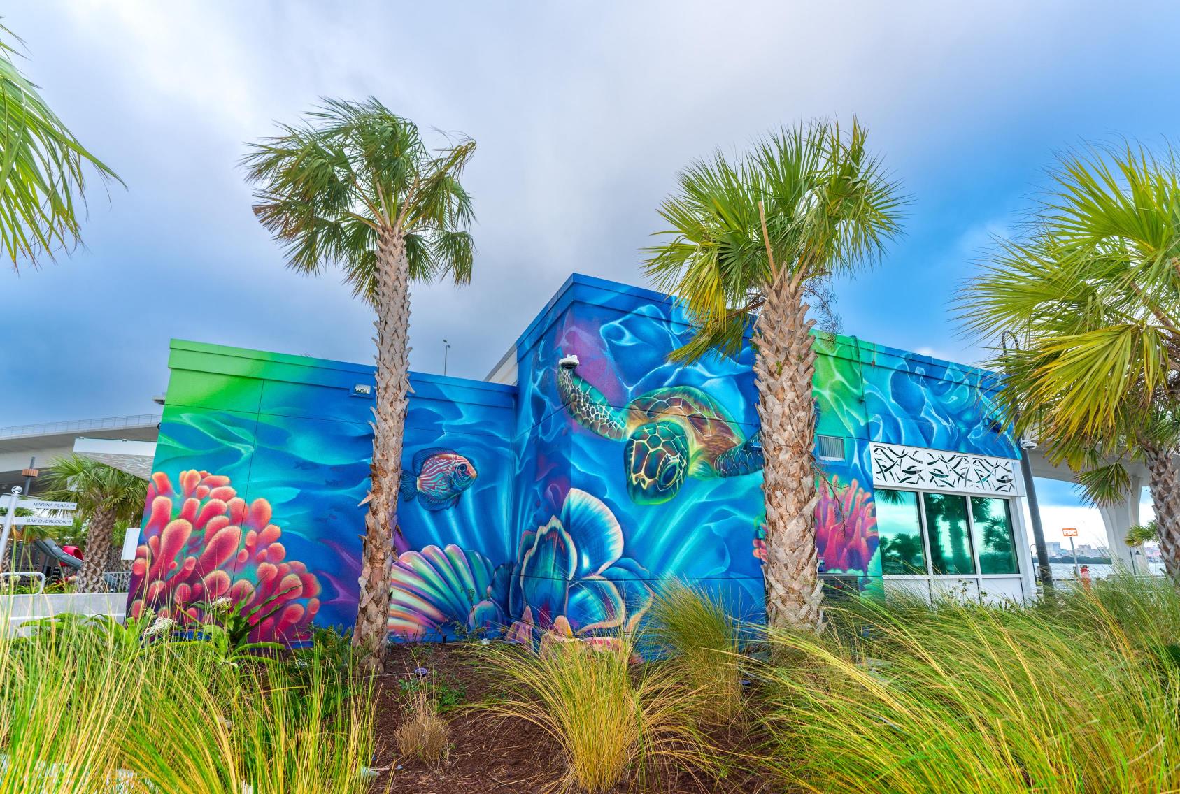 Exterior mural of sea life framed between two palm trees.
