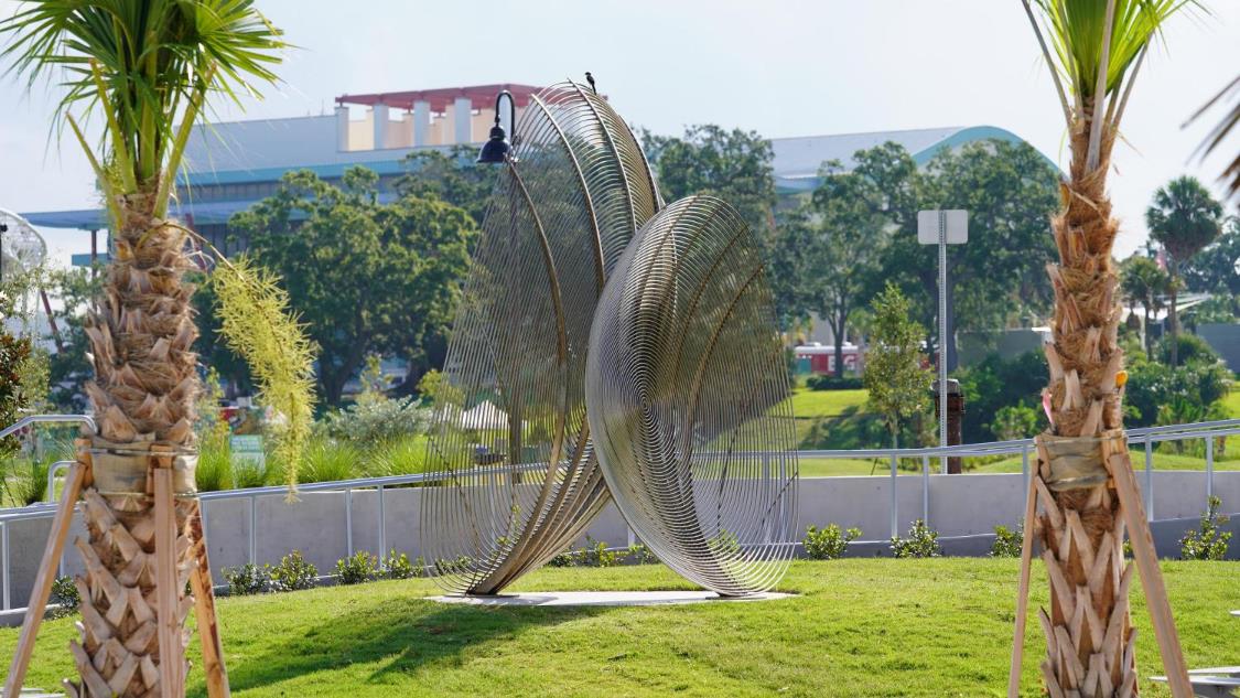 Metal sculpture of two discs seen from far view between trees.