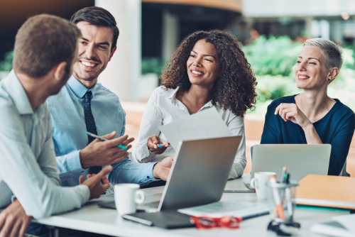 Four people sitting at a table with a laptop talking